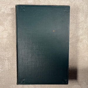 May include: A dark green hardback book with a rectangular shape. The front cover features embossed floral corner details and a small, singular light brown spot near the centre. The spine is visible on the left side of the book.