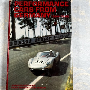 May include: A vintage book titled "Performance Cars From Germany 1894-1965" with a red spine. The cover shows a silver race car with the number 39 on a racetrack. The book's title is in red, and the authors' names are at the bottom.