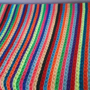 Könnte beinhalten: Eine mehrfarbige gestreifte Decke mit vertikalen Streifen in einer Vielzahl von Farben, darunter Rot, Orange, Gelb, Grün, Blau und Lila. Die Decke besteht aus einem weichen, strukturierten Material. Ein gemütlicher Einrichtungsgegenstand.