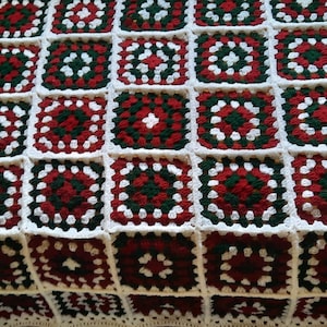 Könnte beinhalten: Eine handgefertigte Häkeldecke mit Patchwork-Design. Die Decke besteht aus zahlreichen quadratischen Motiven in Rot, Grün und Weiß, die ein ansprechendes Muster bilden. Die Quadrate sind in einem rasterartigen Muster angeordnet und zeigen die Handwerkskunst.
