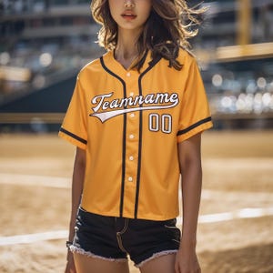 Peut inclure: Un maillot de baseball jaune avec des bordures noires et des lettres blanches. Le maillot porte le texte "Teamname" et le numéro "00" sur le devant.