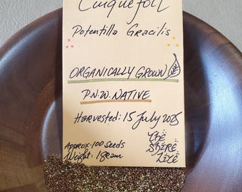 Pode incluir: Uma tigela de madeira cheia de sementes pequenas, com um cartão manuscrito que diz "Slender Cinque foil Potentilla Gracilis ORGANICALLY GROWN P.N.W. NATIVE." O cartão também diz "Harvested: 15 July 2015" e "Approx. 100 Seeds Weight: 18 gramas."