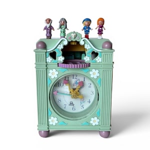 May include: A mint green clock with a white clock face, featuring a floral design and four small figurines on top. The clock has a decorative design with a purple gear and accents.