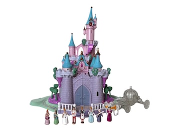May include: A pink and purple toy castle with blue turrets, a clock, and a carriage. The castle has a large front door and is surrounded by small figurines of various characters.