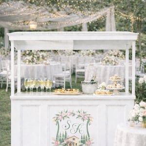 Outdoor wedding bar decorated with personalized watercolor crest monogram featuring florals, initials and romantic venue artwork.