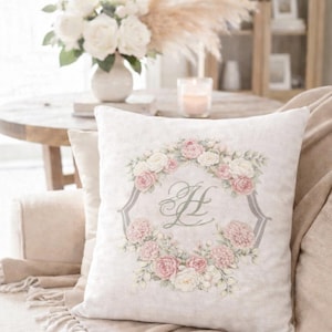 Decorative pillow with a personalized watercolor wedding crest monogram in soft pink florals displayed in a neutral living room.