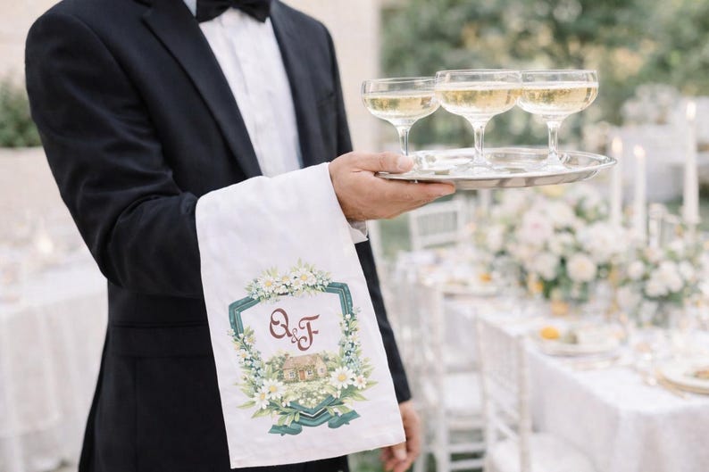 Waiter holding champagne tray with white towel featuring personalized watercolor wedding crest monogram at wedding reception.