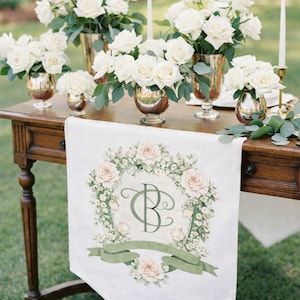 Wooden wedding table with white floral arrangements and a fabric runner featuring a personalized watercolor wedding crest monogram.