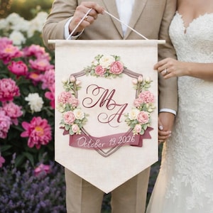 Bride and groom holding a personalized wedding banner with a watercolor crest monogram, pink florals and wedding date.