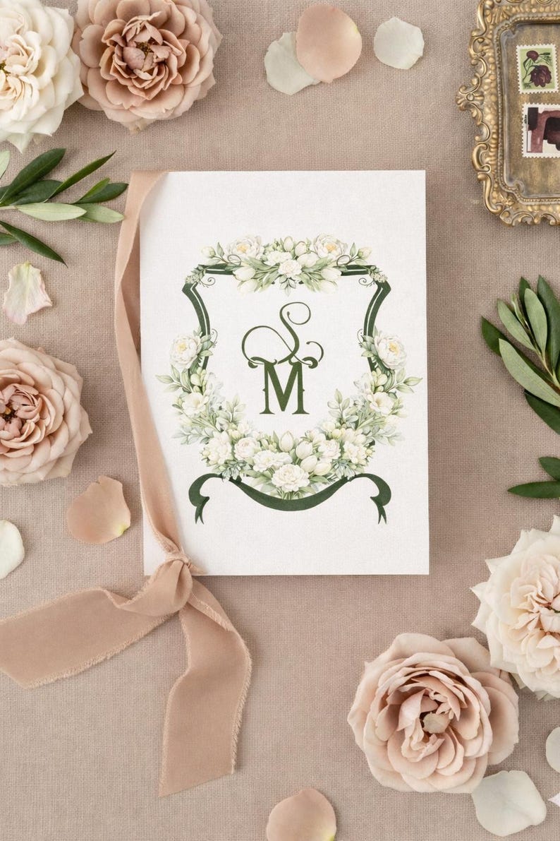 Wedding stationery featuring a personalized watercolor wedding crest monogram surrounded by ribbon, flowers and petals.