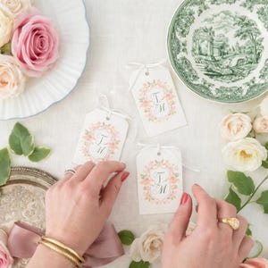 Set of gift tags with a personalized watercolor wedding crest monogram in soft pink florals styled with roses and ribbon.
