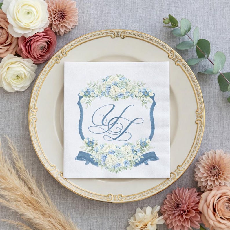 Wedding place setting with a napkin featuring a personalized watercolor wedding crest monogram in blue florals on an elegant plate.