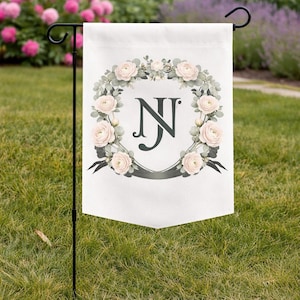 Garden flag with a personalized watercolor wedding crest monogram and soft floral details displayed on a lawn.