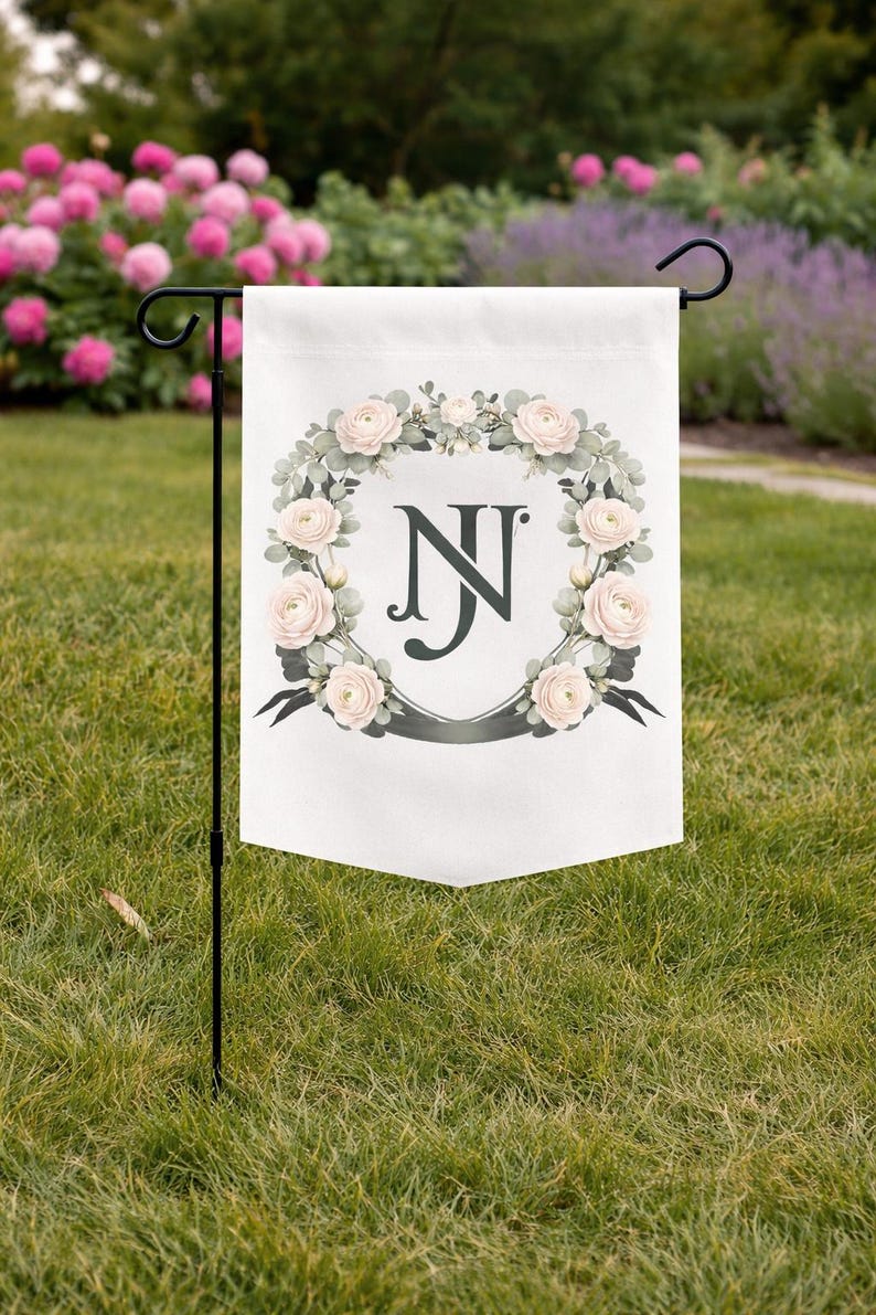 Garden flag with a personalized watercolor wedding crest monogram and soft floral details displayed on a lawn.