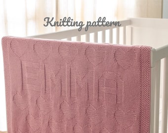 May include: A pink knitted baby blanket with a heart pattern. The blanket is draped over a white crib.