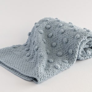 Pu&ograve; includere: Una coperta di maglia blu chiaro piegata, con un motivo a punto riso strutturato. La coperta &egrave; realizzata in materiale morbido ed &egrave; piegata su una superficie bianca. La coperta misura circa 100 cm di lunghezza e 75 cm di larghezza.