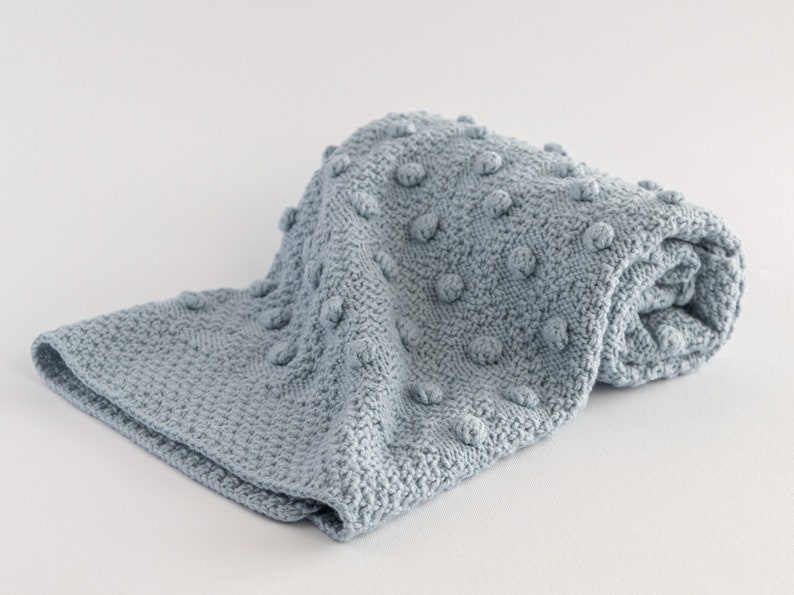 Pu&ograve; includere: Una coperta di maglia blu chiaro piegata, con un motivo a punto riso strutturato. La coperta &egrave; realizzata in materiale morbido ed &egrave; piegata su una superficie bianca. La coperta misura circa 100 cm di lunghezza e 75 cm di larghezza.