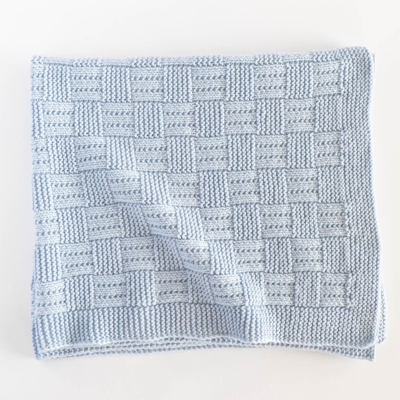 May include: A light blue knitted blanket with a woven basket weave pattern. The blanket is square and has a textured appearance. The soft, cozy blanket is perfect for a baby or child.