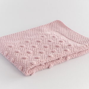 Pu&ograve; includere: Una coperta di maglia rosa chiaro piegata, con una superficie strutturata e un motivo a pois in rilievo. La coperta &egrave; realizzata in materiale morbido ed &egrave; adatta a un bambino. La coperta misura circa 76 cm di lunghezza e 64 cm di larghezza.