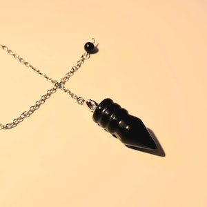 May include: A black pendulum with a silver chain and a black bead at the top.