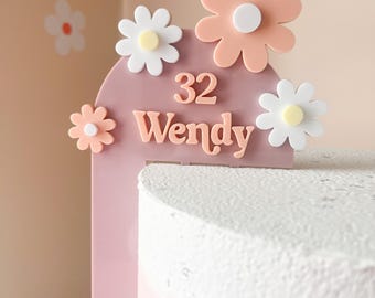 May include: Pink and white cake topper with the number 32 and the name Wendy. The topper is decorated with pink and white flowers.