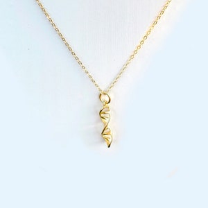 Puede incluir: Un collar de cadena dorada con un colgante de doble hélice dorada.
