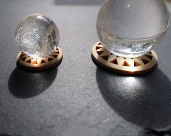 May include: Two clear glass spheres, one large and one small, rest on round, light brown wooden coasters. The coasters have a geometric design cut into them. The spheres appear to be crystal or glass.