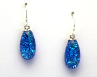 May include: A pair of silver dangle earrings with blue teardrop-shaped glass beads. The glass beads have a textured, iridescent finish.