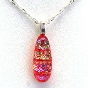 May include: A teardrop-shaped pendant necklace with a red, pink, and gold iridescent glass pendant. The pendant is attached to a silver chain.
