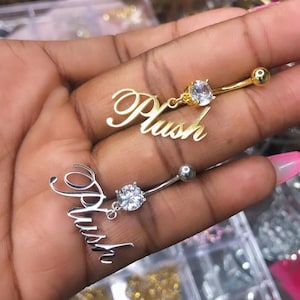 May include: Two belly button rings with a clear rhinestone and the word "Plush" in gold and silver.