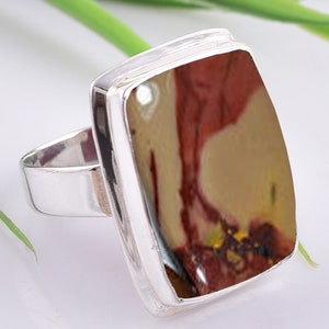 May include: A silver ring featuring a rectangular, multi-coloured stone set in a bezel setting. The stone displays shades of red, brown, and white.