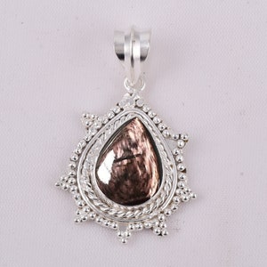 Peut inclure: Un pendentif en argent avec une pierre précieuse irisée en forme de larme sertie dans un cadre en argent avec une bordure décorative. Le pendentif est attaché à une bélière en argent.