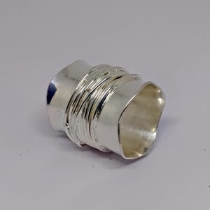 May include: A silver ring with a textured, hammered finish. The ring is made of multiple bands that are twisted and woven together.