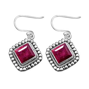 Könnte beinhalten: Ein Paar silberne Ohrhänger mit einem quadratischen roten Edelstein, der in einer silbernen Fassung sitzt. Die Ohrringe haben einen perlenbesetzten Rand und einen einfachen Hakenverschluss.