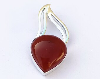 May include: A silver pendant with a red carnelian gemstone in a teardrop shape. The pendant has a delicate, flowing design.