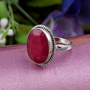Può includere: Un anello d'argento con una grande pietra preziosa rossa di forma ovale incastonata in una fascia d'argento ritorta.
