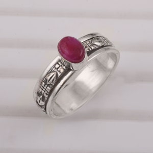 Puede incluir: Un anillo de plata con una piedra ovalada roja y diseños florales intrincados en la banda.