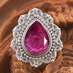 May include: A silver ring with an ornate design features a large, pear-shaped, pink gemstone.