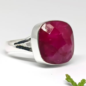 May include: A silver ring with a large, faceted, cushion-cut ruby gemstone. The ruby is a deep, rich red color.