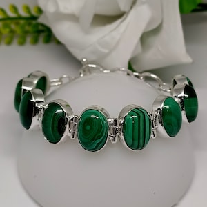 Op de afbeelding: Een zilveren armband met ovale malachietstenen. De stenen zijn diep groen van kleur met draaiende patronen.