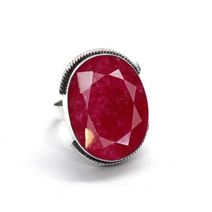May include: A silver ring with a large, faceted, red ruby gemstone.