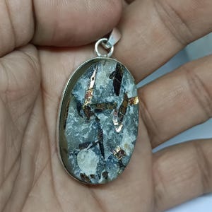 May include: Silver pendant with an oval-shaped stone featuring a mix of black, white, and gold flecks.