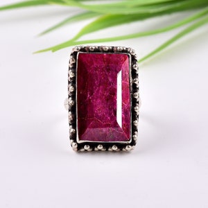 May include: A silver ring with a large, rectangular, pink ruby gemstone set in a beaded bezel.