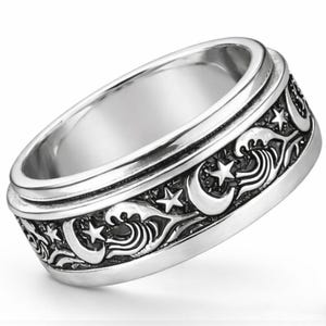 May include: A silver-colored ring with a detailed design of waves, stars, and crescent moons. The ring has a textured band with a spinning outer ring. The ring is made of a shiny, metallic material.