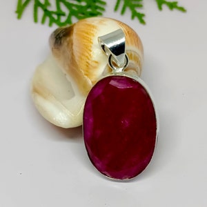 Peut inclure: Un pendentif en argent avec une grande pierre de rubis facetée de forme ovale. Le rubis est d'une couleur rouge foncé et riche.