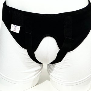 Op de afbeelding: Zwarte steungordel met verstelbare banden en een klittenbandsluiting. De gordel heeft een label met de tekst "LJC, Lumbosacral Support Care, CE, Small".