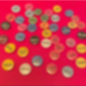 Könnte beinhalten: Eine Ansammlung farbenfroher, runder Objekte mit Text, die auf einer roten Oberfläche verstreut sind. Die Objekte haben verschiedene Farben, darunter Gelb, Blau, Grün und Braun. Der Text scheint auf die Oberfläche jedes Objekts gedruckt zu sein.