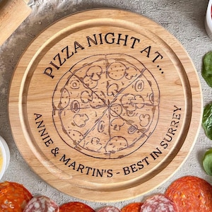 May include: A circular wooden pizza board with a laser-etched pizza design. The text "PIZZA NIGHT AT... ANNIE & MARTIN'S - BEST IN SURREY" is etched around the pizza graphic. Ingredients like cheese, pepperoni, and spinach surround the board.