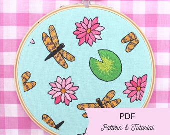 May include: Embroidered hoop art featuring a blue background with pink water lilies, yellow dragonflies, and a green lily pad. The hoop is made of wood and has a metal screw on the top. The text "PDF Pattern & Tutorial" is visible at the bottom of the image.