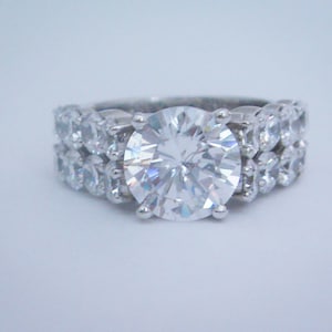 May include: A silver ring with a large, clear, round-cut center stone surrounded by smaller, clear stones.
